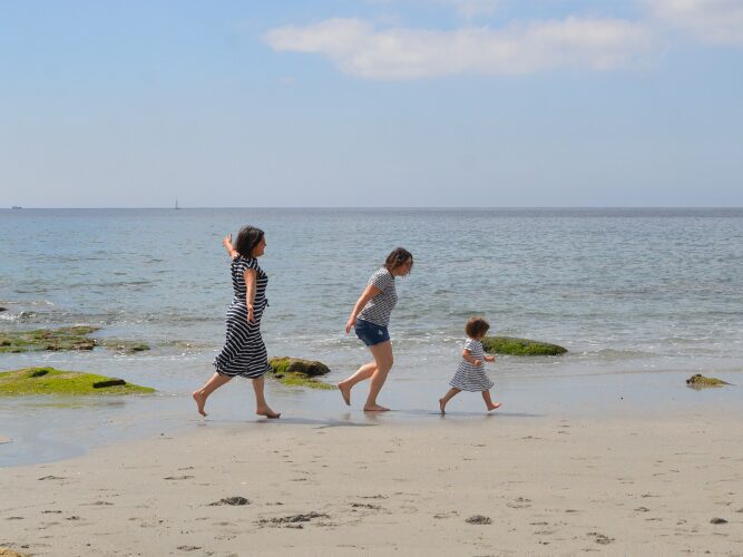 Un enfant qui court sur la plage avec ses deux mamans.